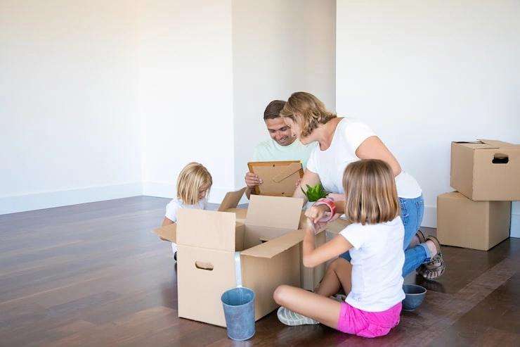 padres-e-hijos-felices-desempacando-cosas-nuevo-apartamento-vacio-sentados-suelo-sacando-objetos-cajas-abiertas_74855-10018